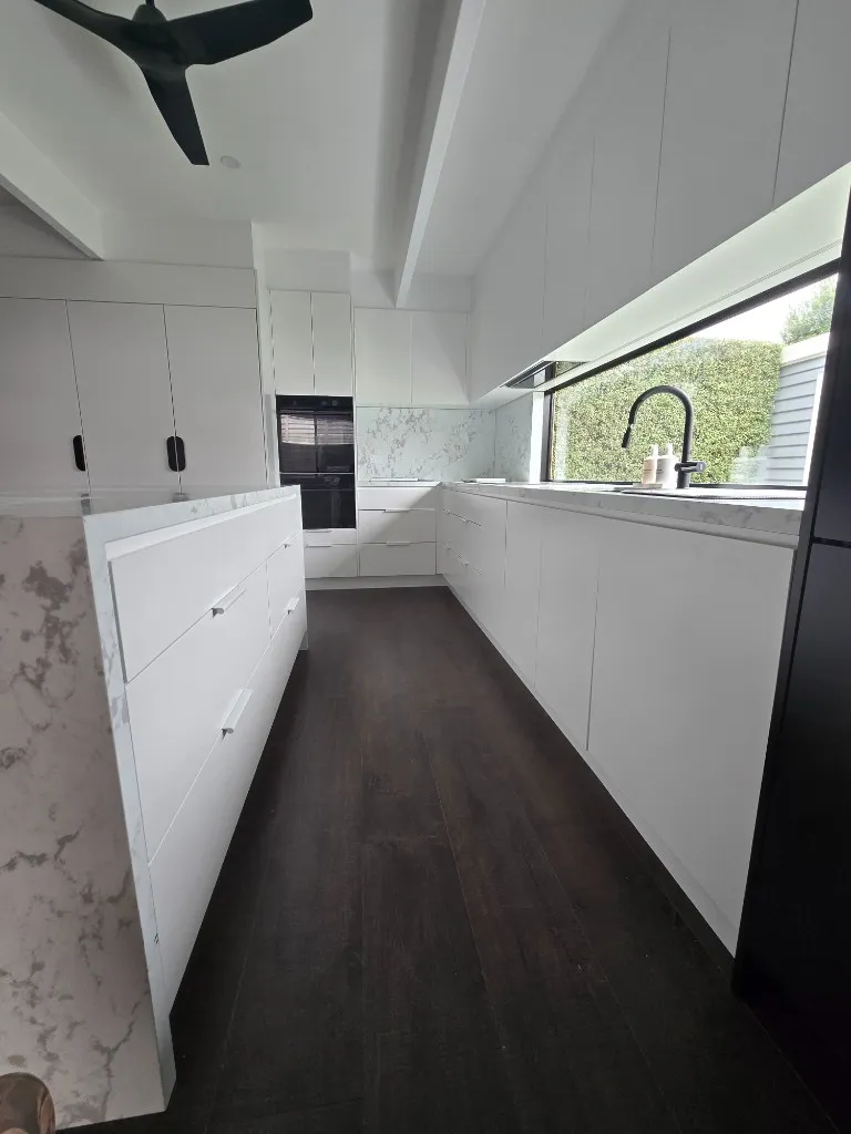 White handleless kitchen with marble splashback and dark timber floor
