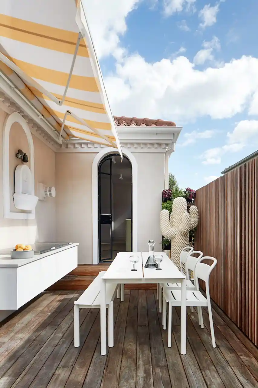 Compact white outdoor bench with sink under a striped awning on a timber deck