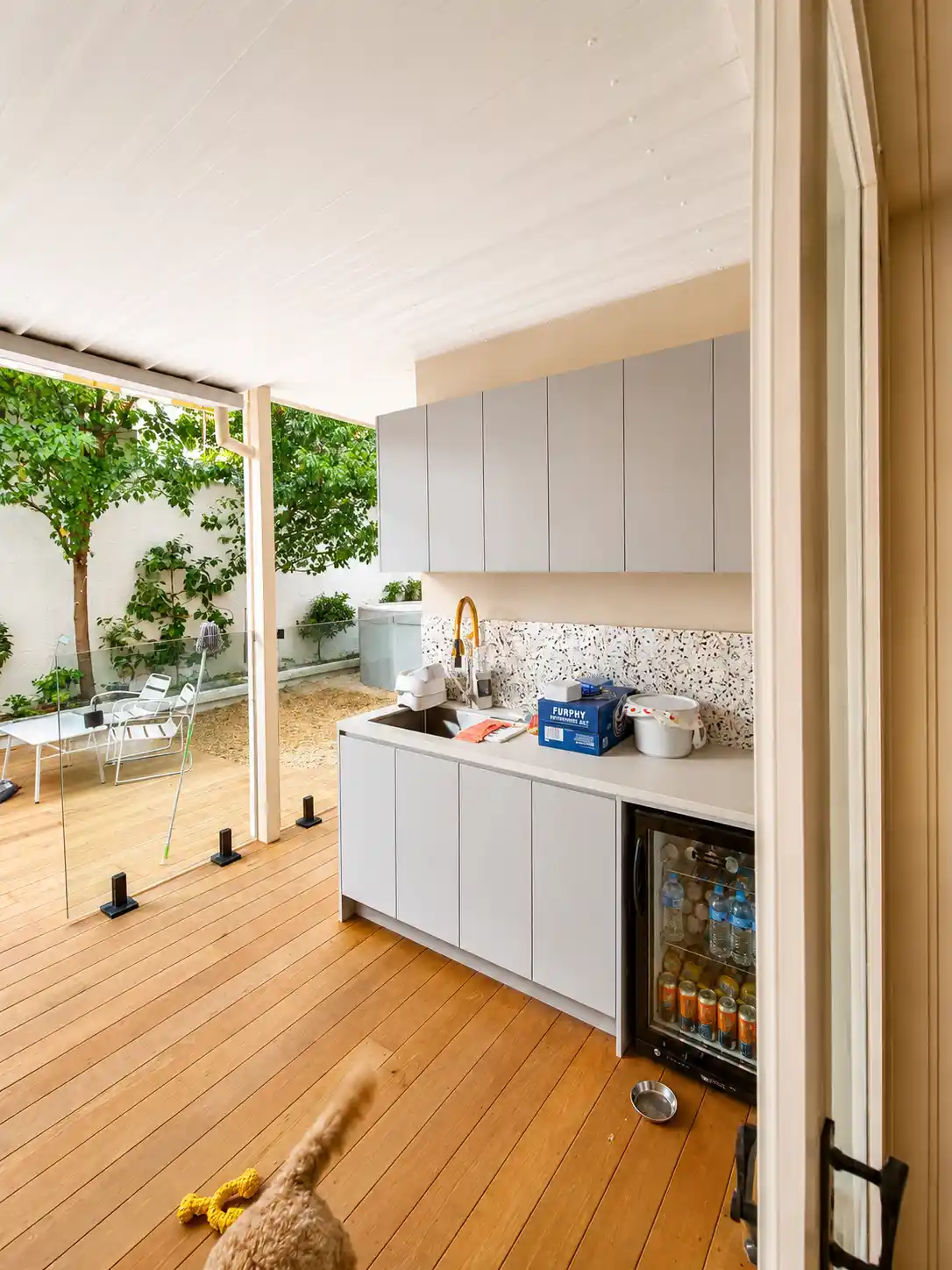 Covered alfresco kitchen with grey cabinetry, terrazzo splashback and bar fridge
